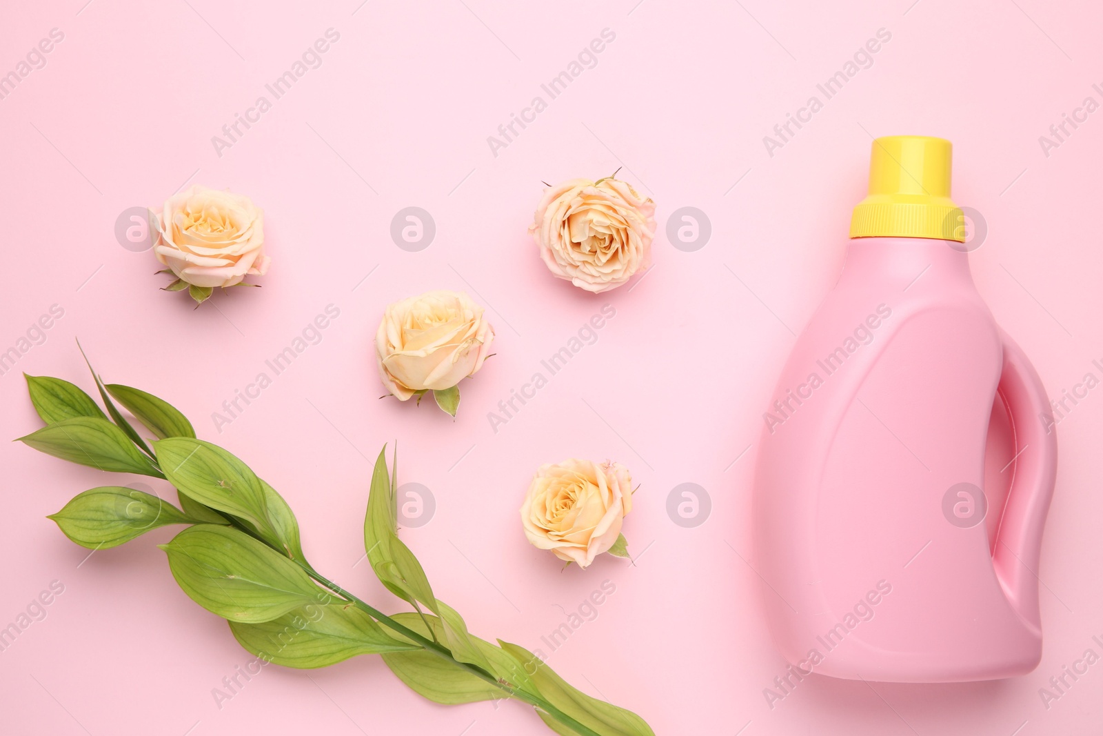 Photo of Bottle of laundry detergent and flowers on pink background, closeup