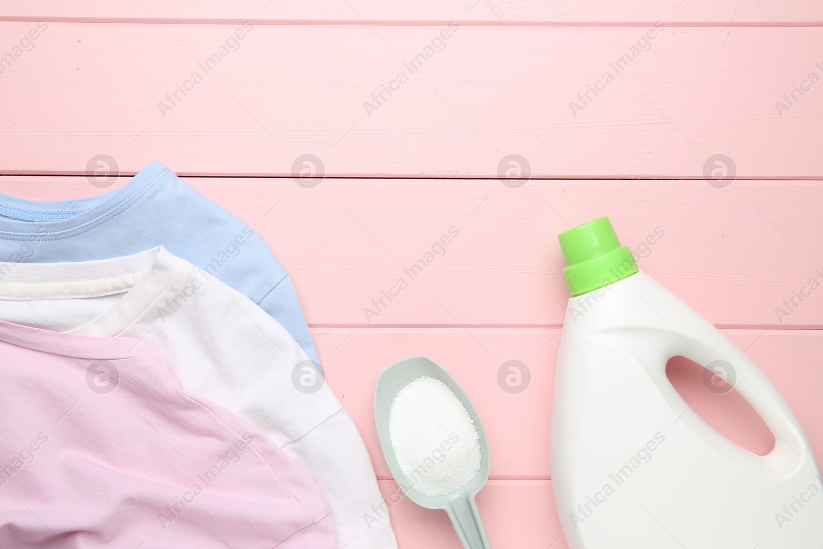 Photo of Laundry detergents and t-shirts on pink wooden table, flat lay