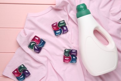 Photo of Laundry detergent in bottle, pods and t-shirt on pink wooden table, top view