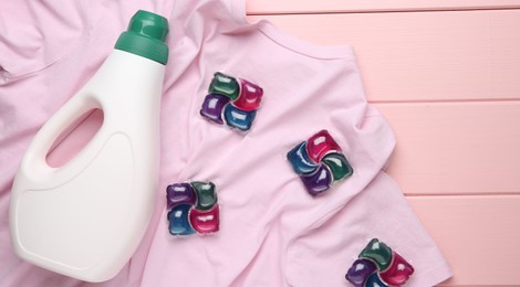 Photo of Laundry detergent in bottle, pods and t-shirt on pink wooden table, top view