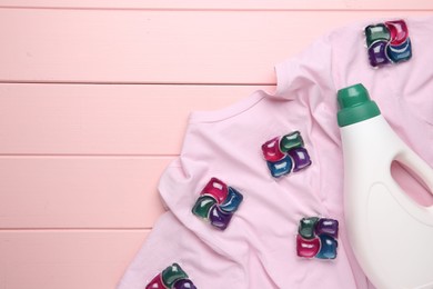 Photo of Laundry detergent in bottle, pods and t-shirt on pink wooden table, top view. Space for text