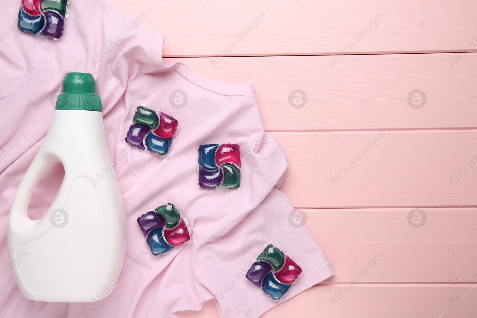 Photo of Laundry detergent in bottle, pods and t-shirt on pink wooden table, top view. Space for text