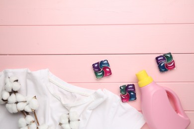 Photo of Laundry detergent in bottle, pods, cotton flowers and t-shirt on pink wooden table, flat lay