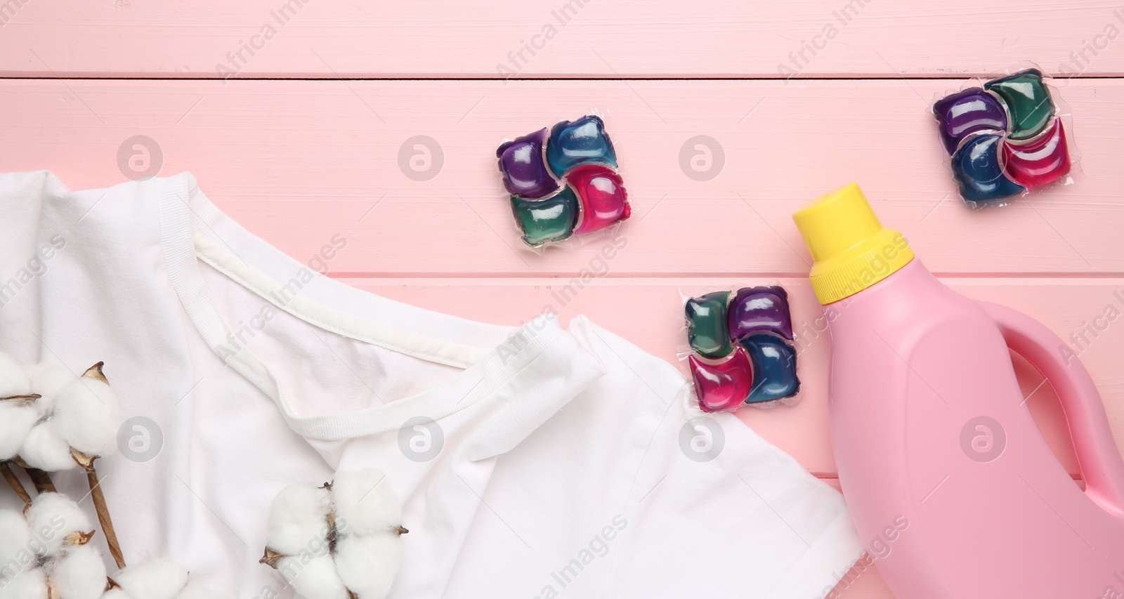 Photo of Laundry detergent in bottle, pods, cotton flowers and t-shirt on pink wooden table, flat lay