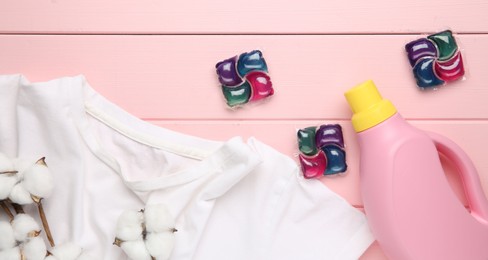 Photo of Laundry detergent in bottle, pods, cotton flowers and t-shirt on pink wooden table, flat lay