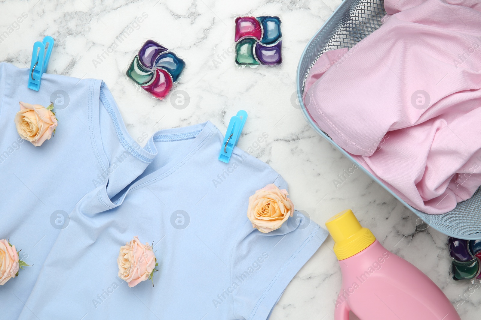 Photo of Flat lay composition with laundry detergents, rose flowers and t-shirts on white marble table