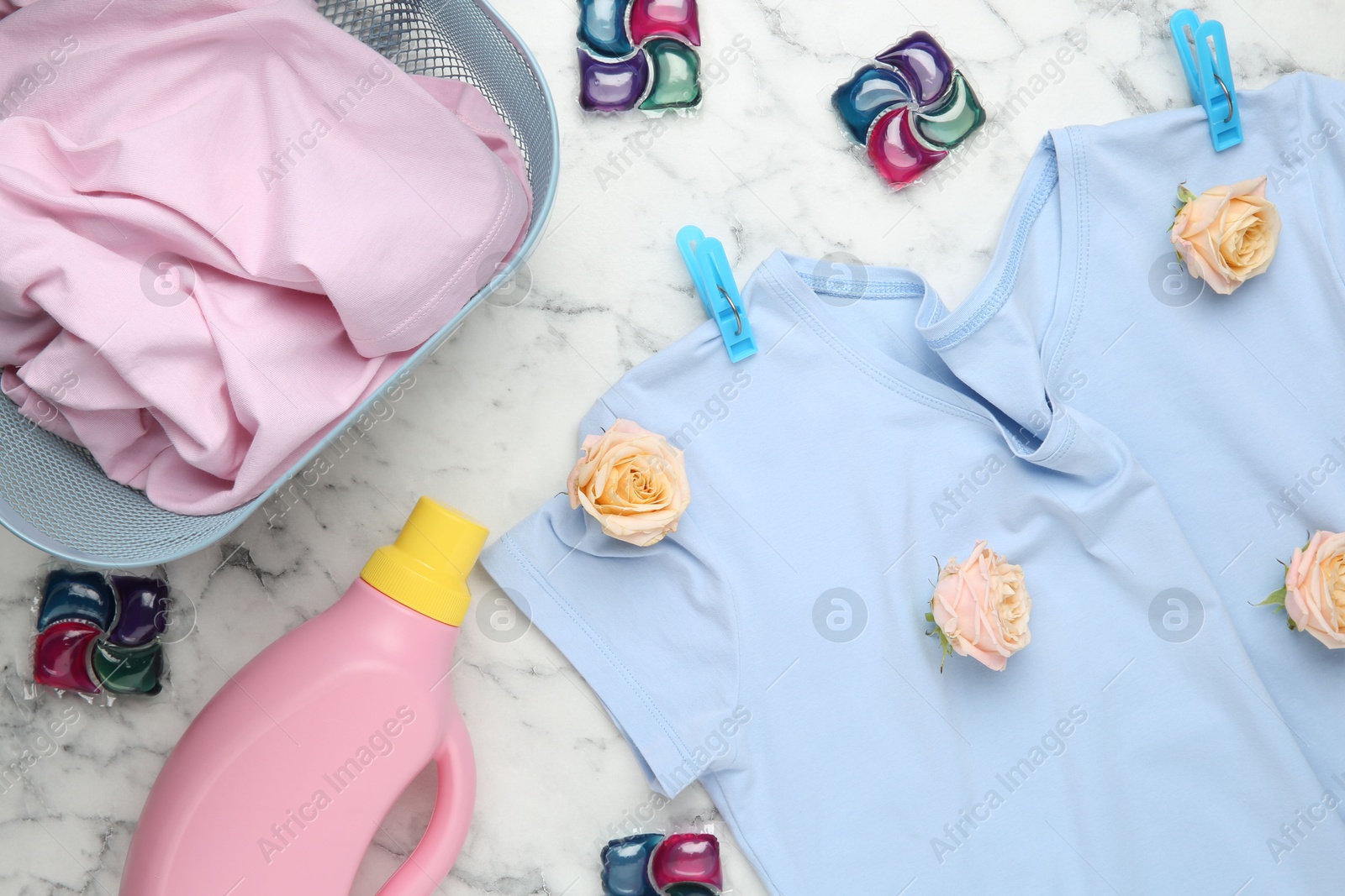 Photo of Flat lay composition with laundry detergents, rose flowers and t-shirts on white marble table