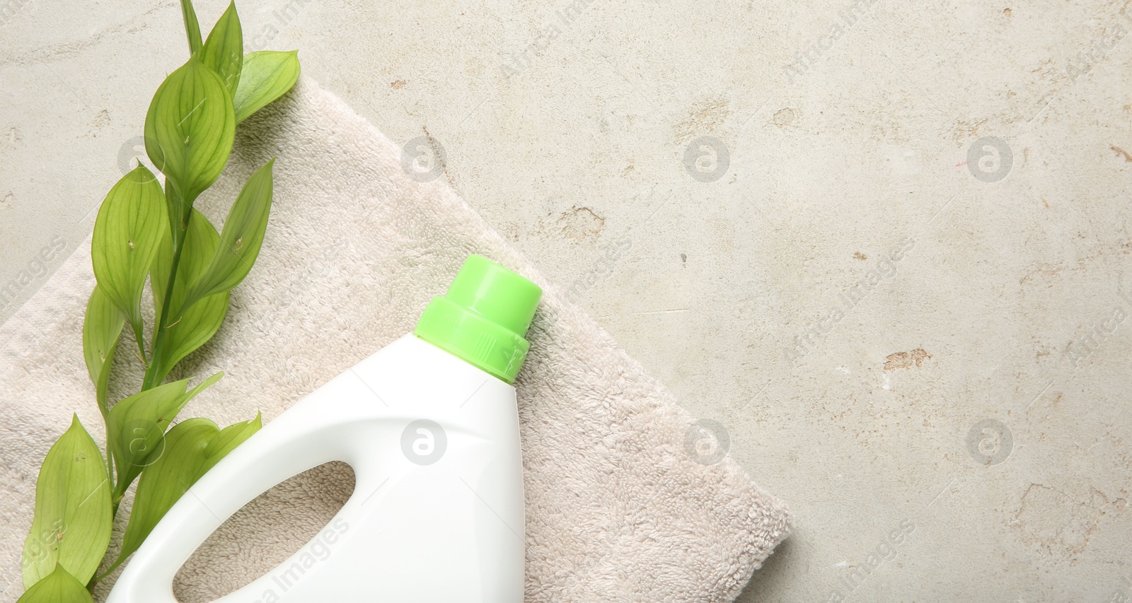 Photo of Laundry detergent in bottle, branch and towel on grey textured table, top view. Space for text