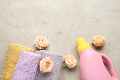 Photo of Laundry detergent in bottle, rose flowers and towels on grey textured table, flat lay. Space for text