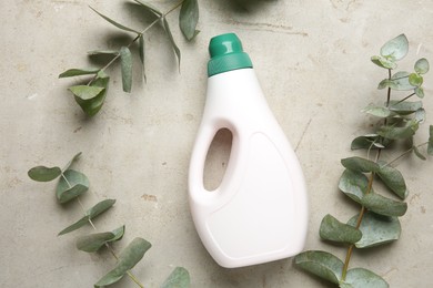 Photo of Laundry detergent in bottle among eucalyptus branches on grey textured table, flat lay