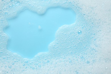 Photo of Washing laundry. White foam with bubbles on light blue background, top view