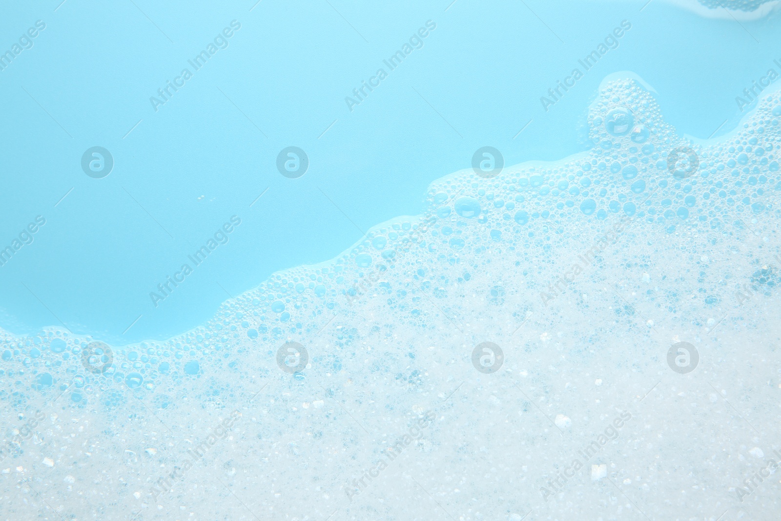 Photo of Washing laundry. White foam with bubbles on light blue background, top view