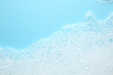 Washing laundry. White foam with bubbles on light blue background, top view