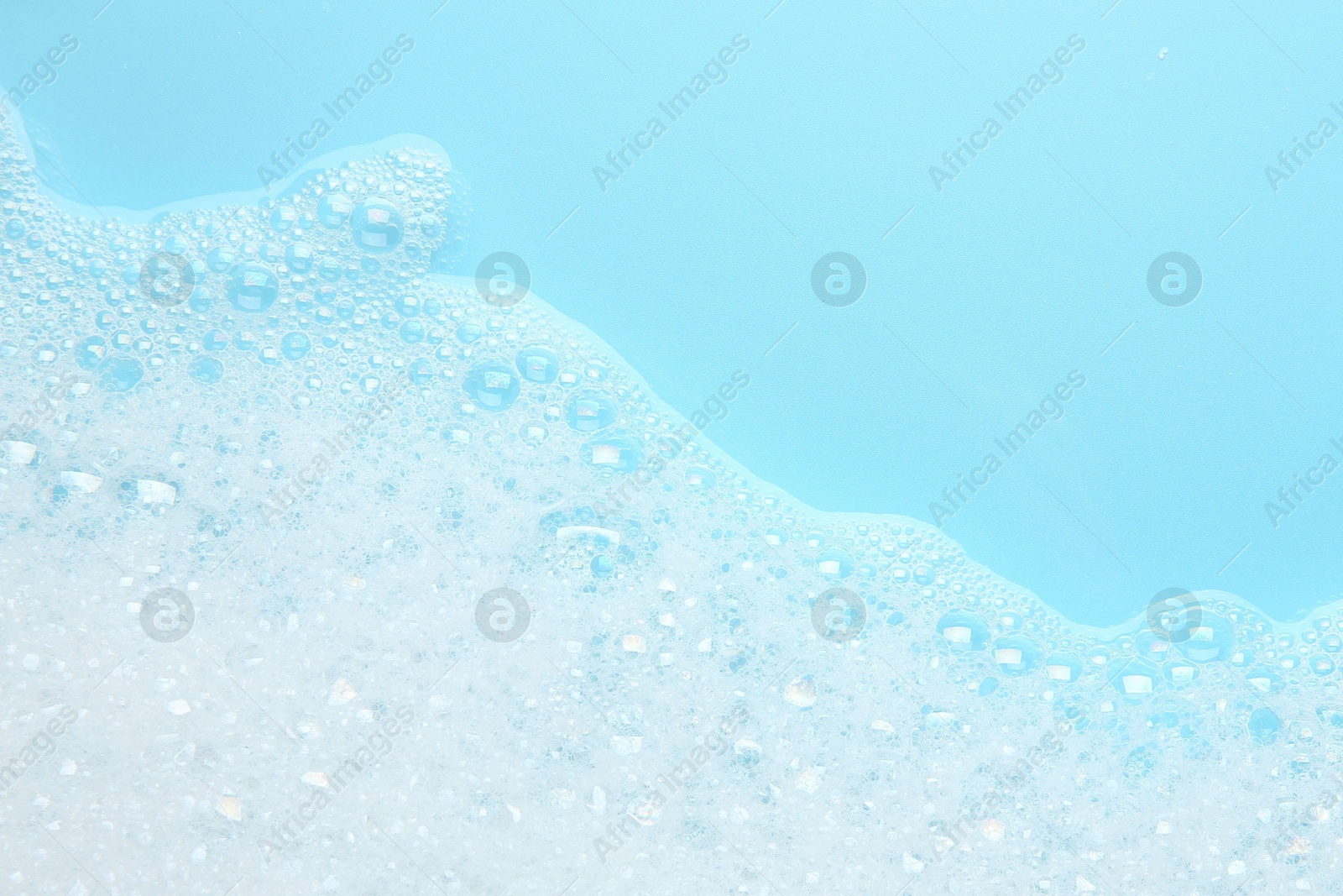 Photo of Washing laundry. White foam with bubbles on light blue background, top view