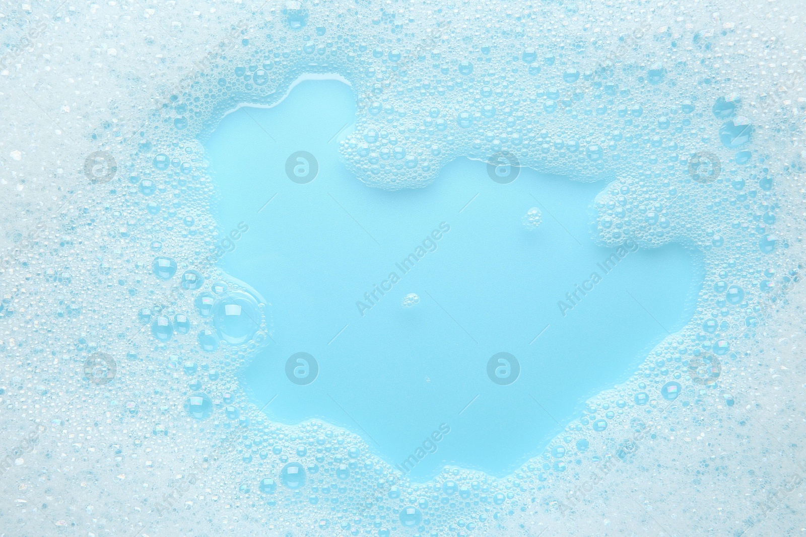 Photo of Washing laundry. White foam with bubbles on light blue background, top view