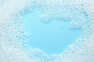 Photo of Washing laundry. White foam with bubbles on light blue background, top view