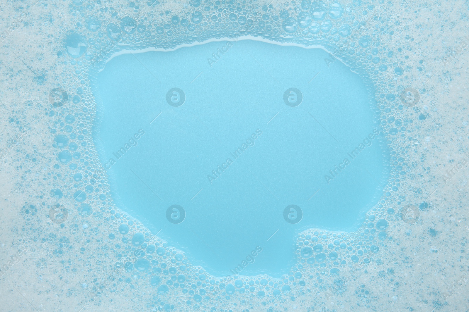 Photo of Washing laundry. White foam with bubbles on light blue background, top view