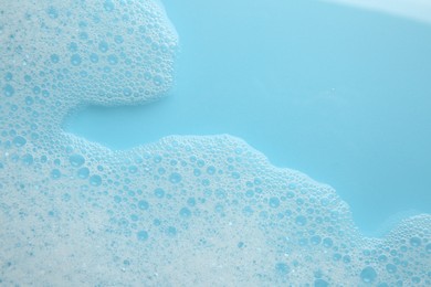 Photo of Washing laundry. White foam with bubbles on light blue background, top view. Space for text