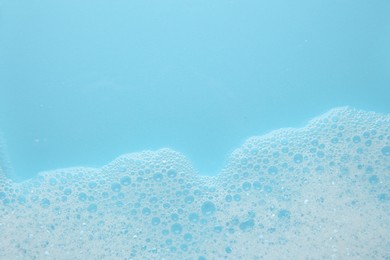 Photo of Washing laundry. White foam with bubbles on light blue background, top view. Space for text