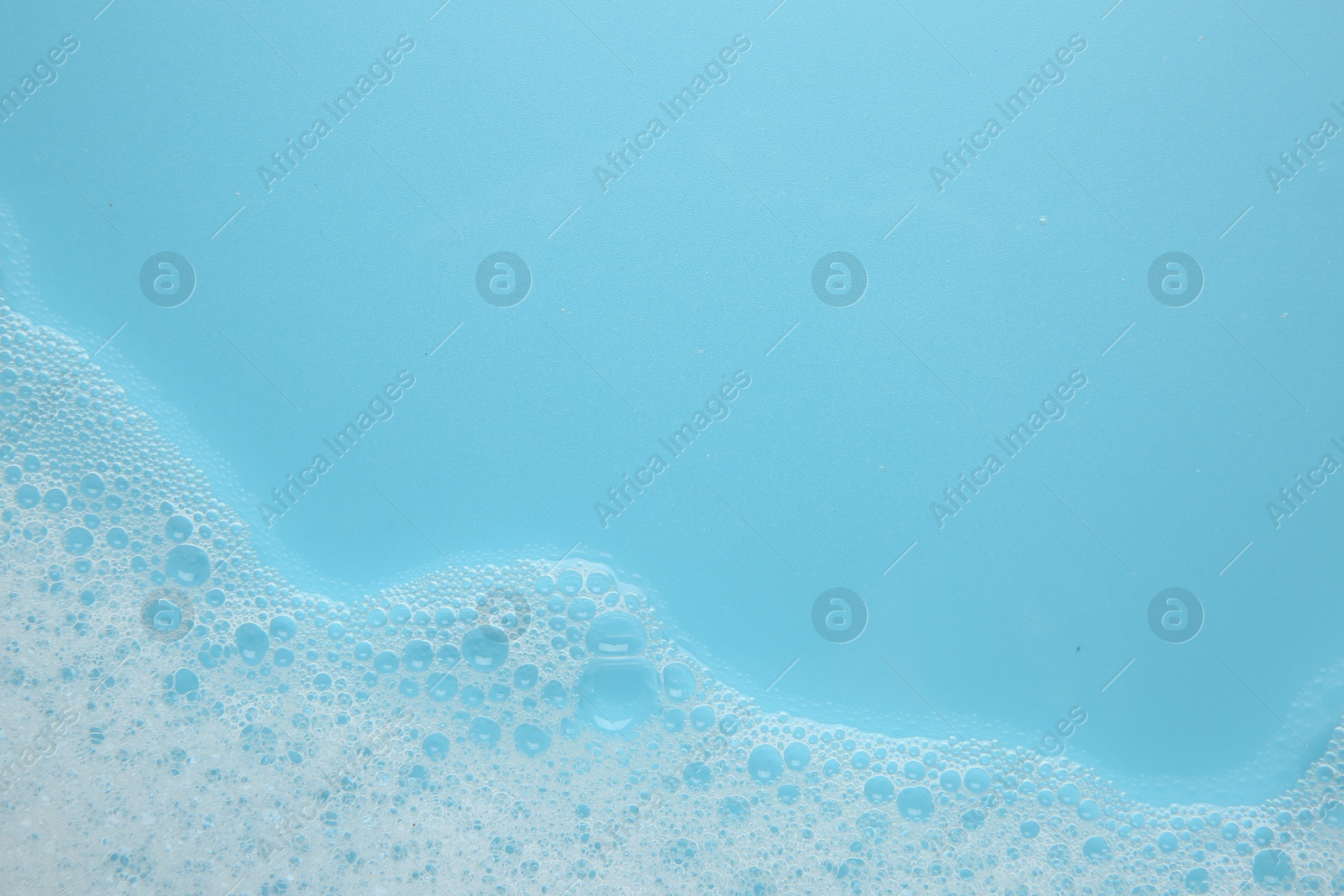 Photo of Washing laundry. White foam with bubbles on light blue background, top view. Space for text