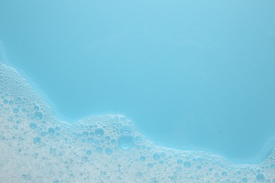 Photo of Washing laundry. White foam with bubbles on light blue background, top view. Space for text