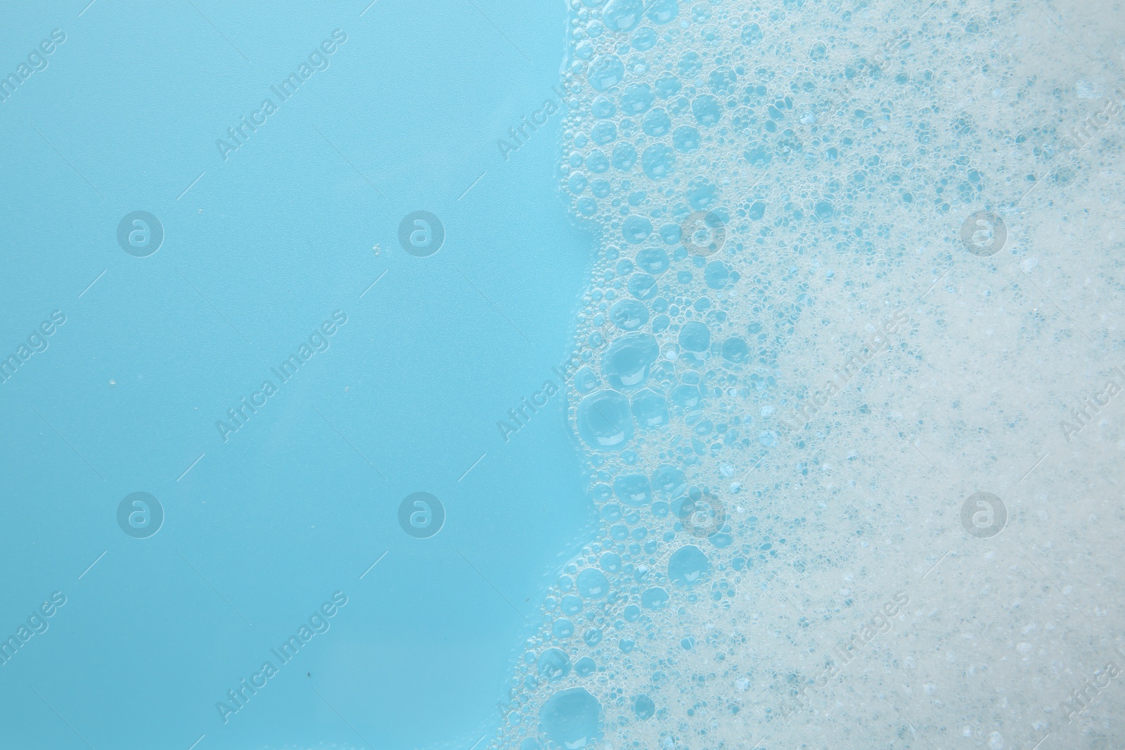 Photo of Washing laundry. White foam with bubbles on light blue background, top view. Space for text