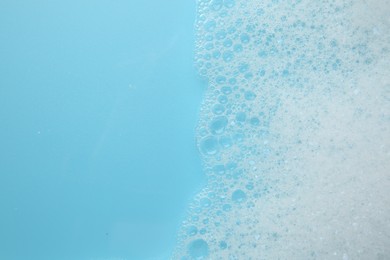 Photo of Washing laundry. White foam with bubbles on light blue background, top view. Space for text