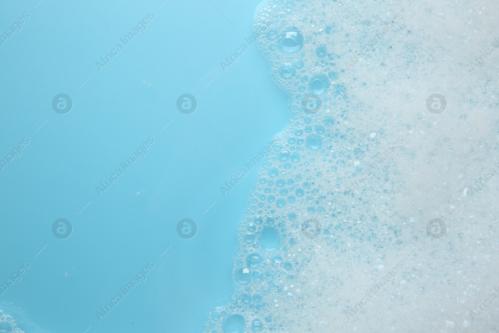 Photo of Washing laundry. White foam with bubbles on light blue background, top view. Space for text