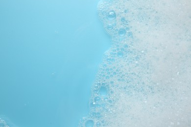 Photo of Washing laundry. White foam with bubbles on light blue background, top view. Space for text