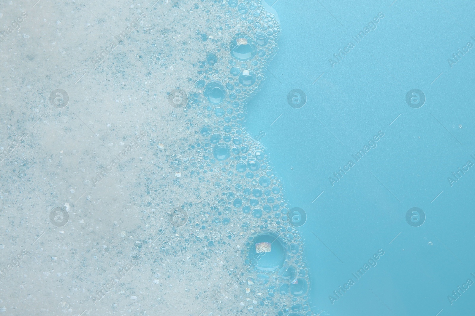 Photo of Washing laundry. White foam with bubbles on light blue background, top view. Space for text