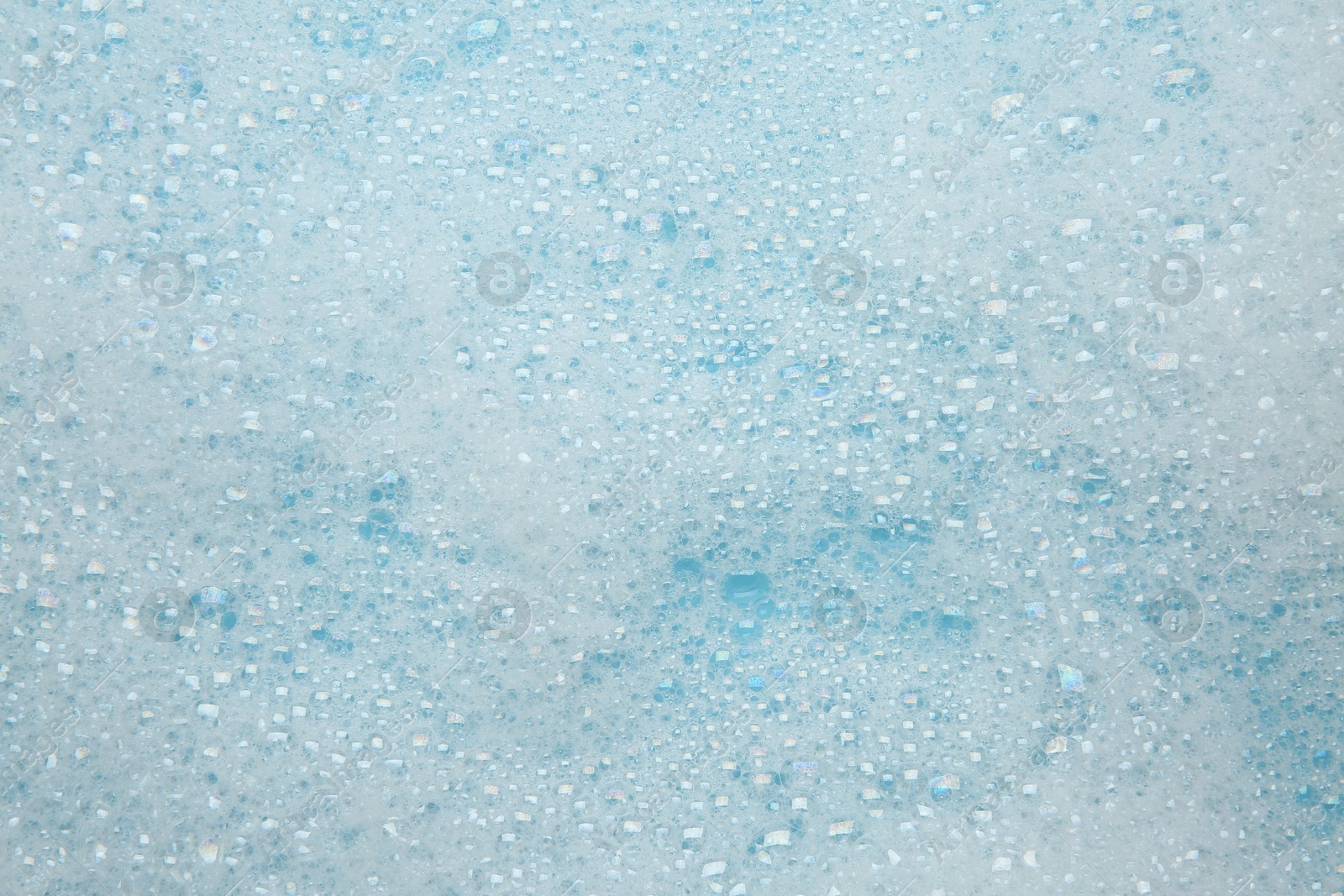 Photo of Washing laundry. White foam with bubbles on light blue background, top view