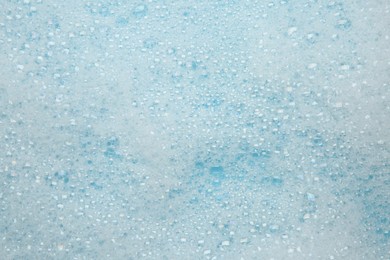 Photo of Washing laundry. White foam with bubbles on light blue background, top view