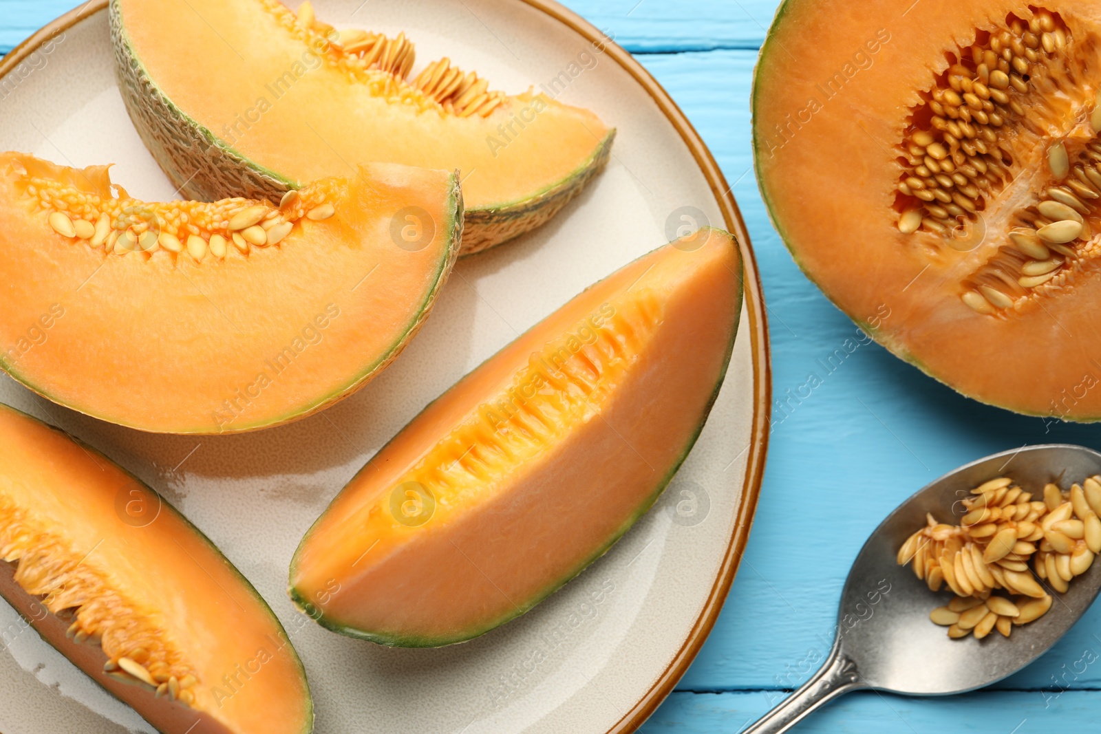 Photo of Cut ripe Cantaloupe melon and spoon with seeds on light blue wooden table, flat lay