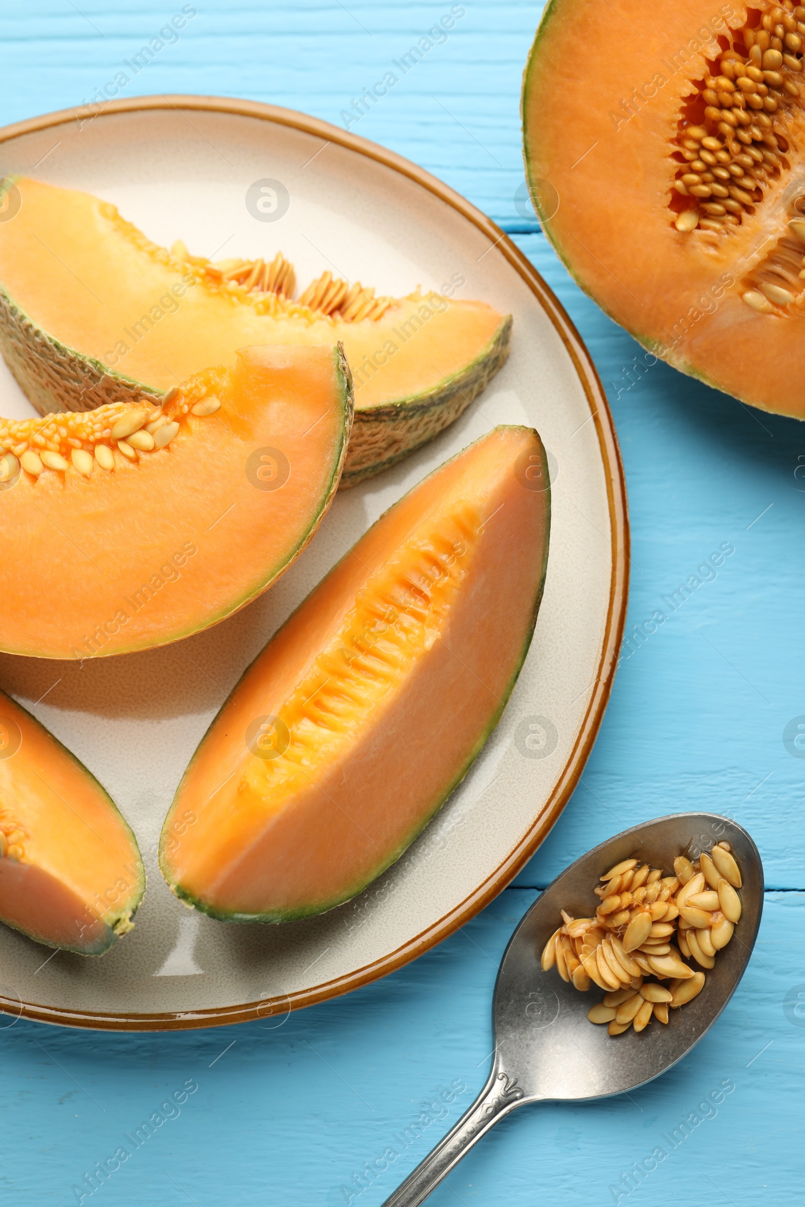 Photo of Cut ripe Cantaloupe melon and spoon with seeds on light blue wooden table, flat lay