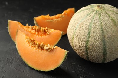 Photo of Cut and whole ripe Cantaloupe melons on dark textured table, closeup