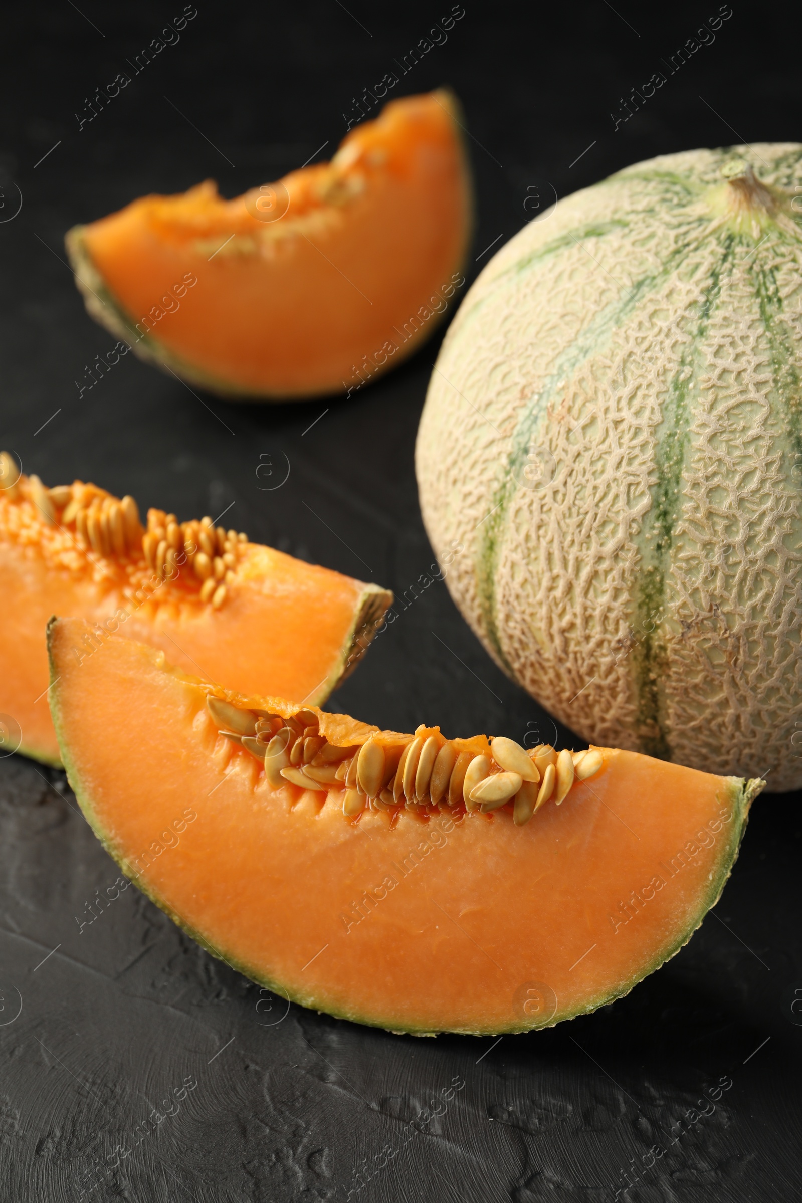 Photo of Cut and whole ripe Cantaloupe melons on dark textured table, closeup