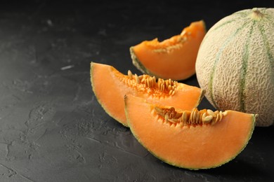 Photo of Cut and whole ripe Cantaloupe melons on dark textured table, closeup. Space for text