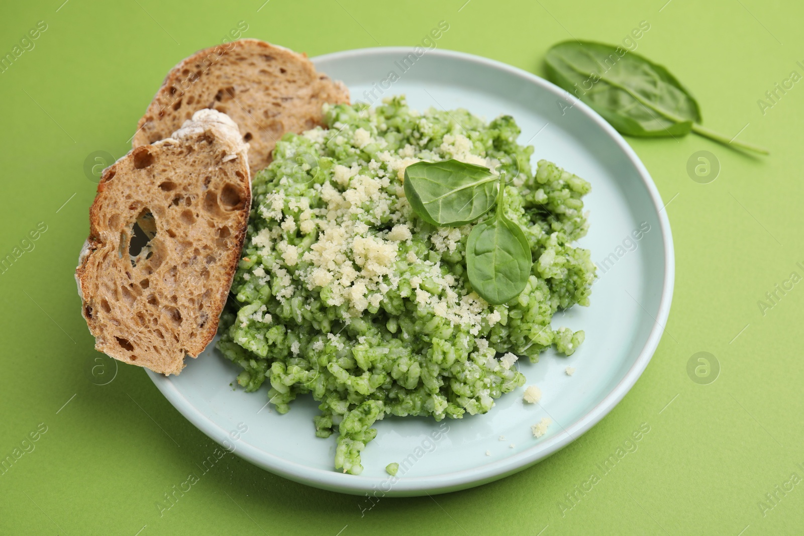 Photo of Tasty spinach risotto and bread on light green background, closeup