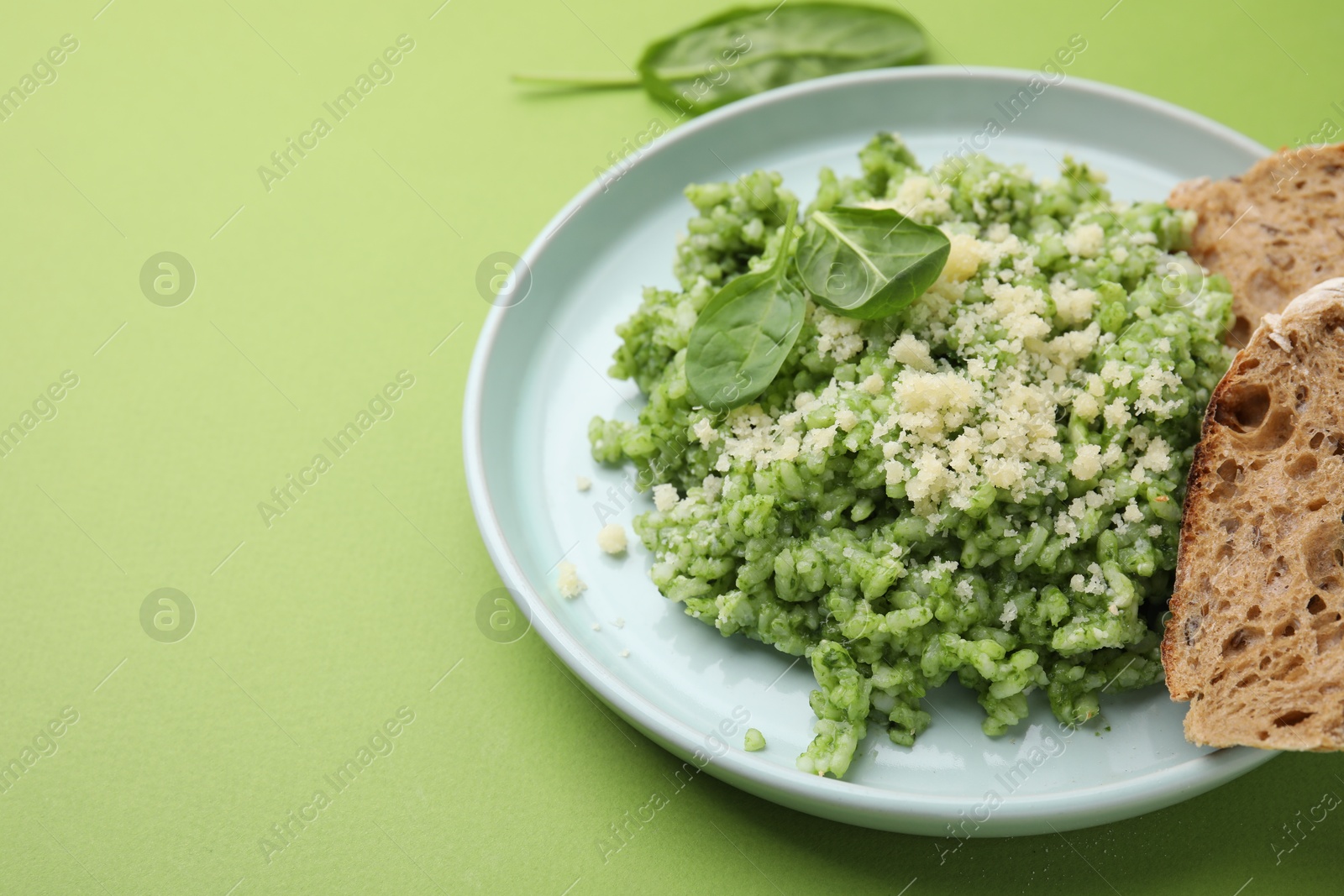 Photo of Tasty spinach risotto and bread on light green background, closeup. Space for text