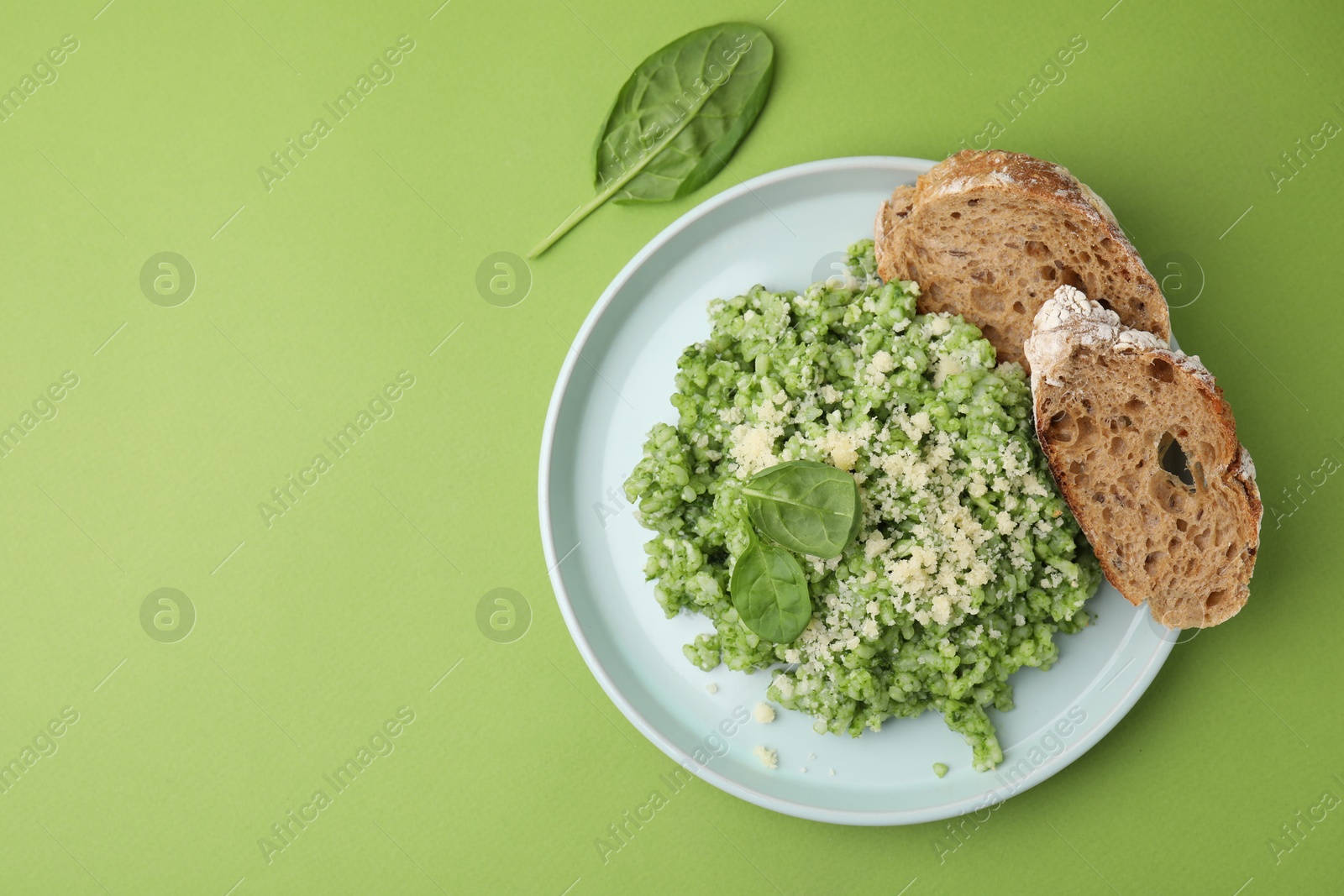 Photo of Tasty spinach risotto and bread on light green background, top view. Space for text