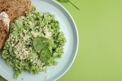 Photo of Tasty spinach risotto and bread on light green background, top view. Space for text