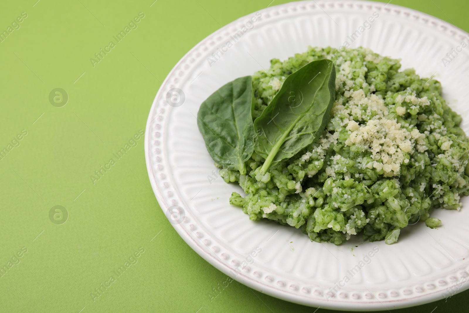 Photo of Tasty spinach risotto on light green background, closeup. Space for text