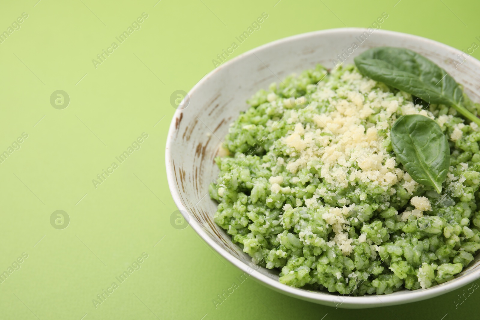 Photo of Tasty spinach risotto on light green background, closeup. Space for text