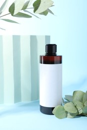 Shampoo in bottle and green eucalyptus leaves on light blue background