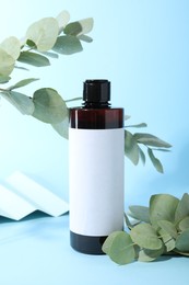 Photo of Shampoo in bottle and green eucalyptus leaves on light blue background