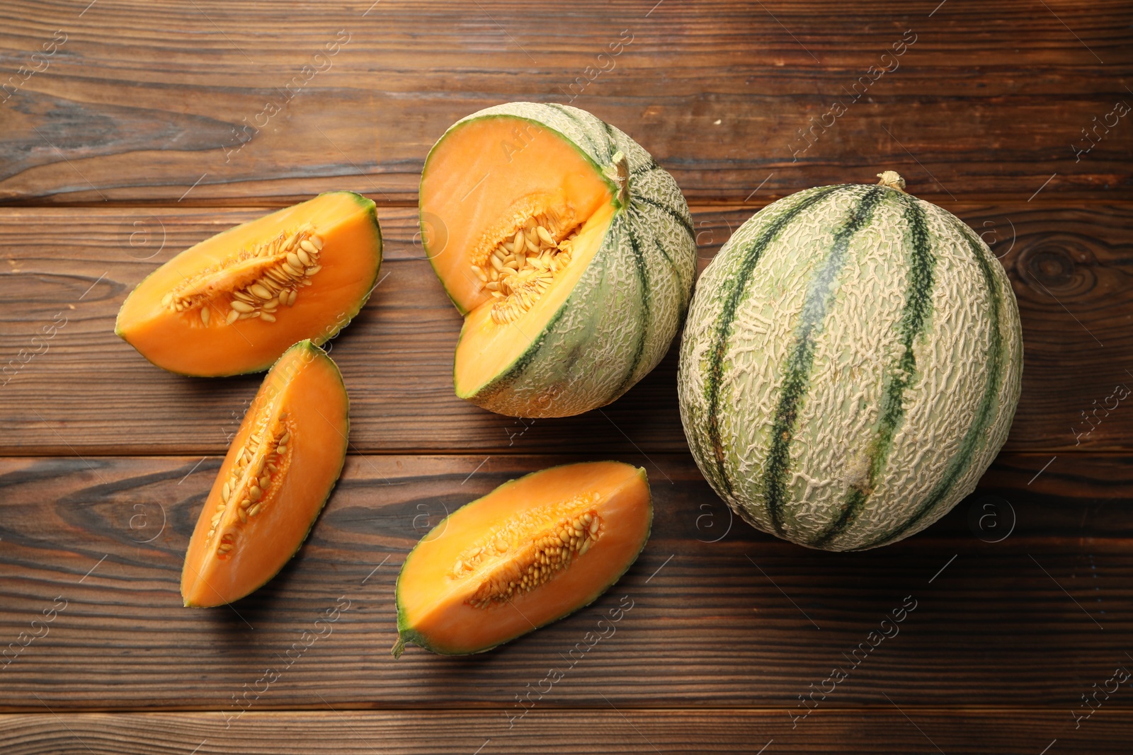 Photo of Cut and whole Cantaloupe melons on wooden table, flat lay