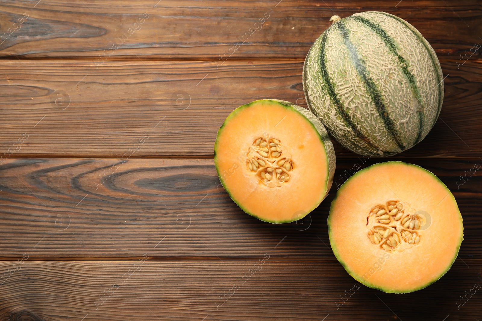 Photo of Cut and whole Cantaloupe melons on wooden table, flat lay. Space for text