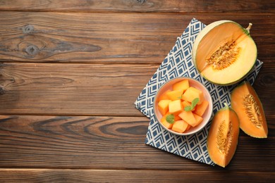 Pieces of Cantaloupe melon and mint in bowl on wooden table, flat lay. Space for text