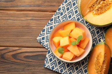 Pieces of Cantaloupe melon and mint in bowl on wooden table, flat lay. Space for text