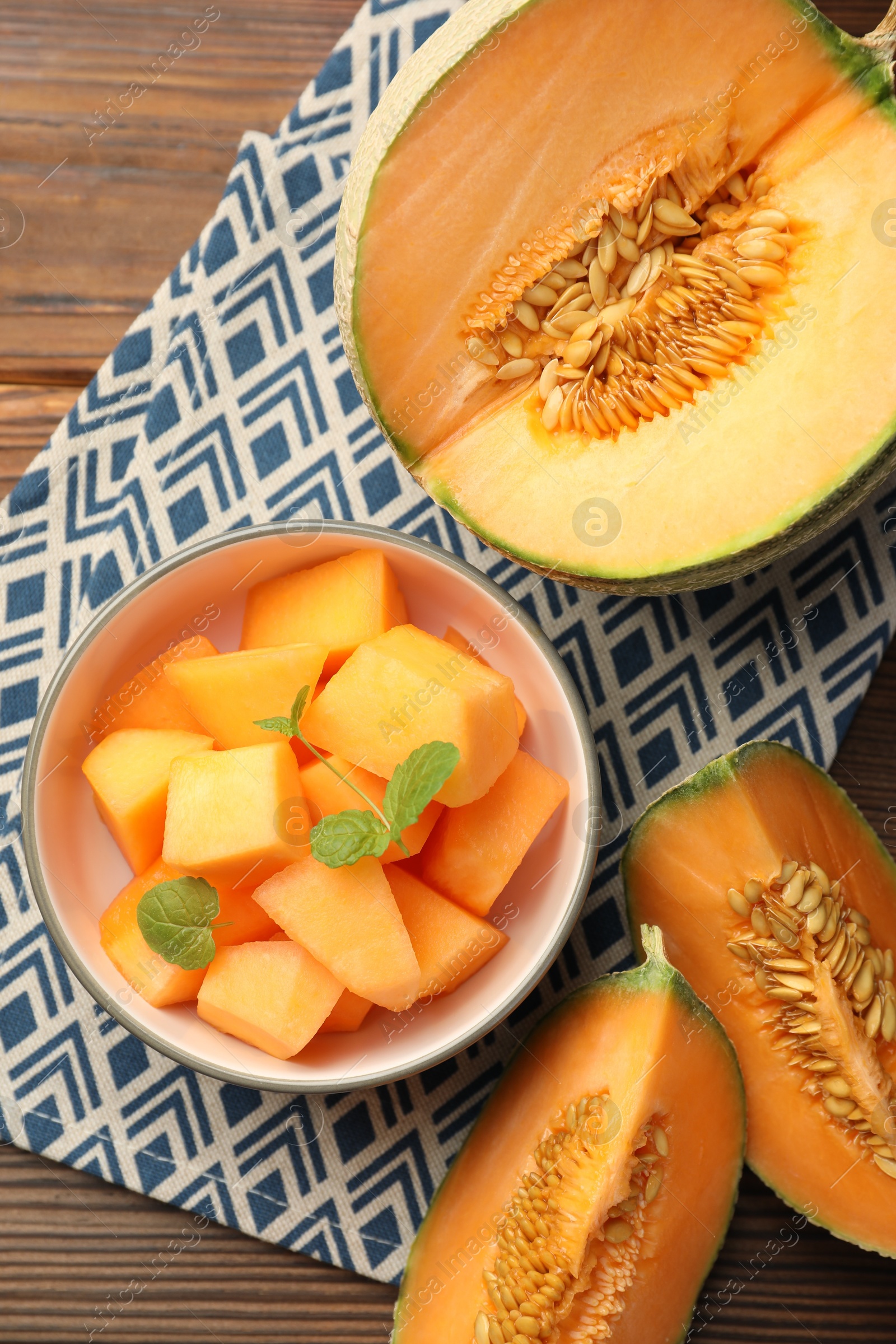 Photo of Pieces of Cantaloupe melon and mint in bowl on wooden table, flat lay